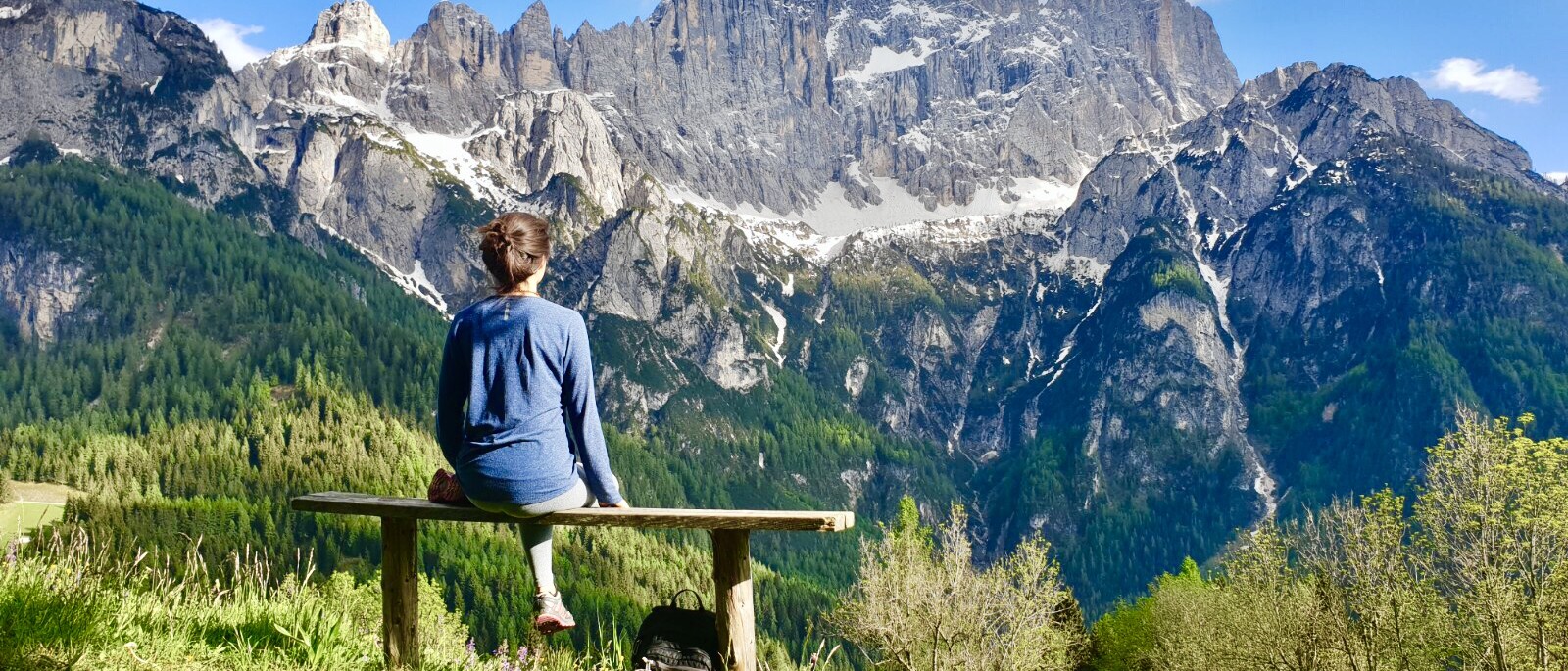 Estate sulle Dolomiti - ragazza seduta su una panchina che guarda le dolomiti illuminate dal sole